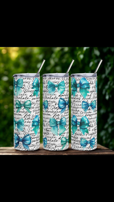 Three tumblers with blue/green bow design on a wooden surface with greenery in the background