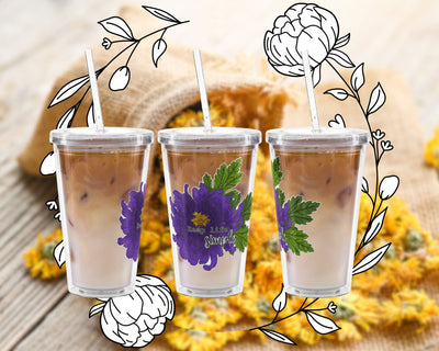 Three clear tumblers with purple floral designs on a wooden surface with flowers and leaves.