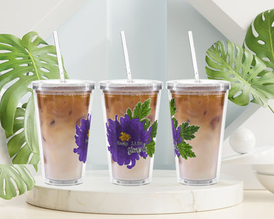 Three clear tumblers with floral designs on a white surface with green leaves in the background