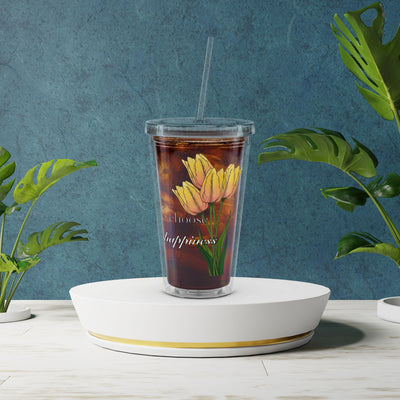 Tumbler with floral design and text on a white stand against a blue wall with plants.