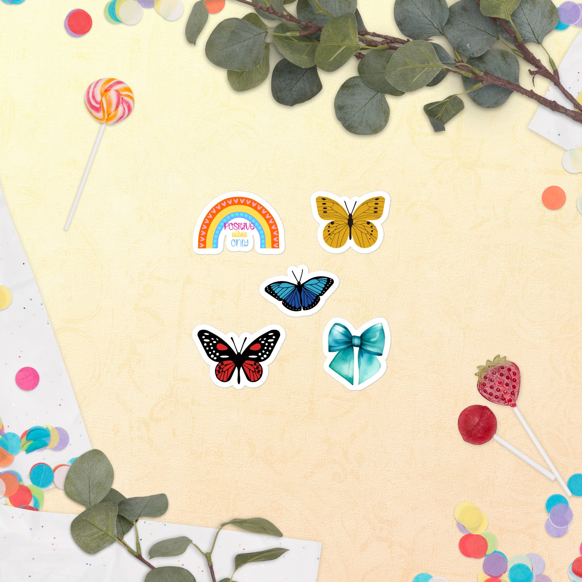Kiss Cut rainbow, butterfly and bow stickers on a yellow page with leaves and lollipops with a white background.