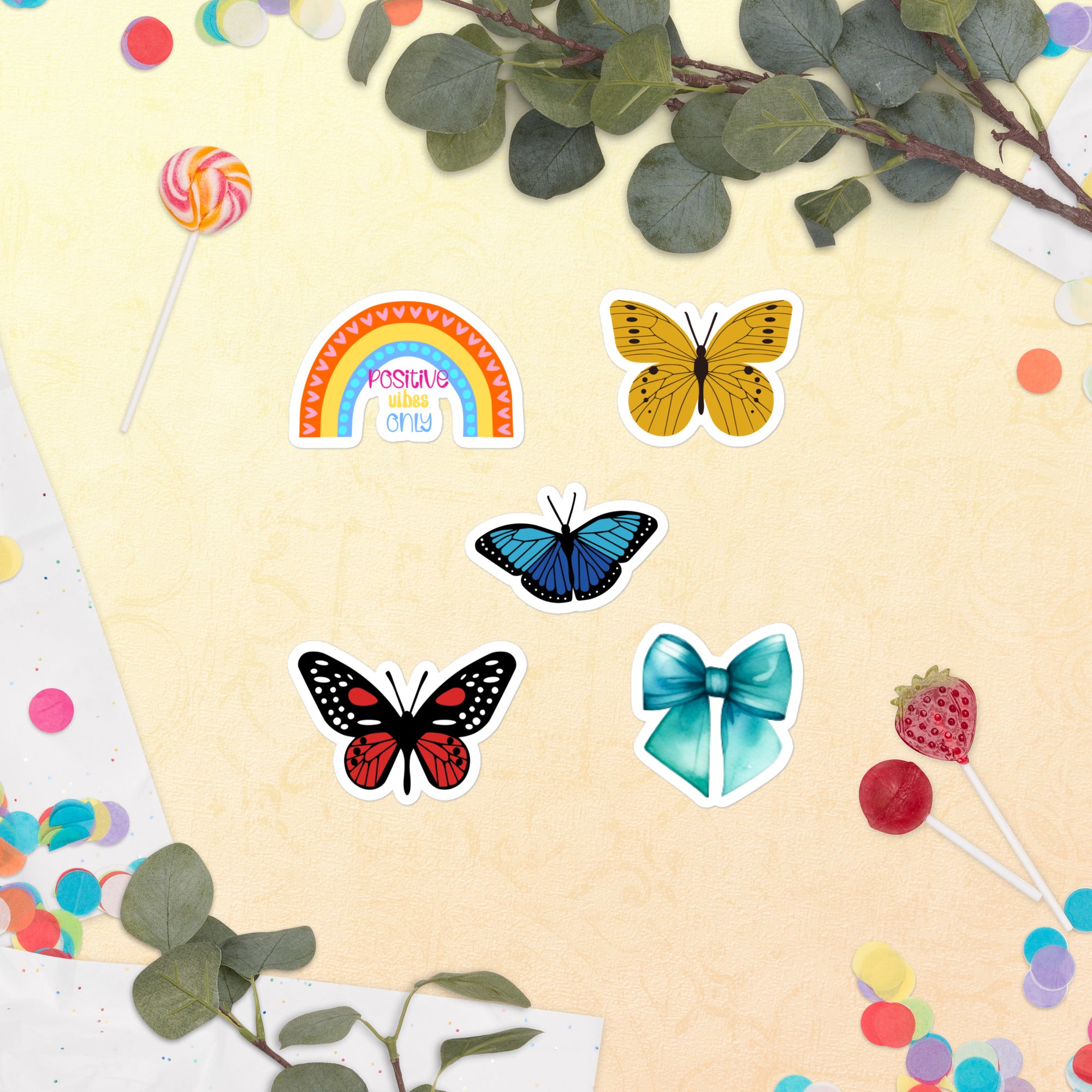 Colourful butterfly and rainbow stickers on a yellow background with leaves and lollipops.