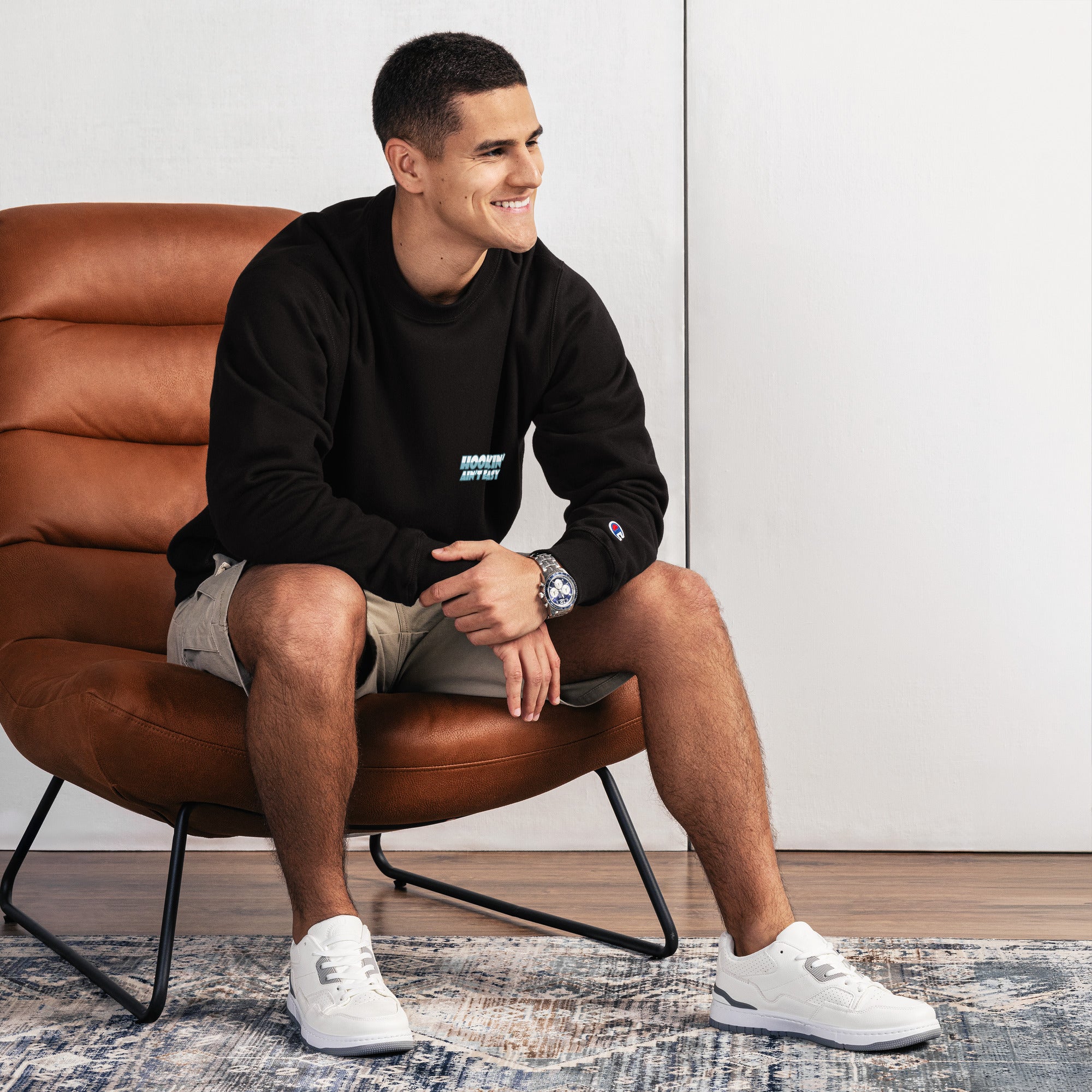 Man sitting on a brown leather chair wearing a black sweatshirt and white sneakers.