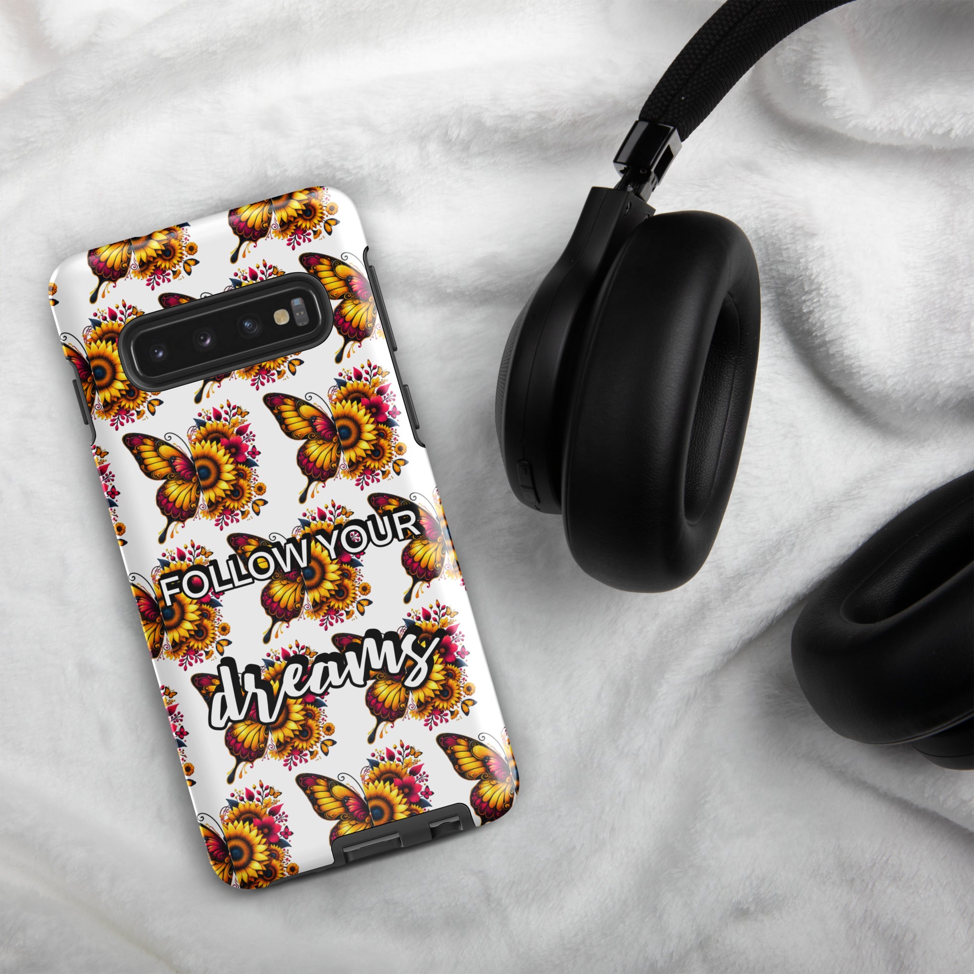 Phone case with butterfly design and 'Follow Your Dreams' text on a marble surface with headphones.
