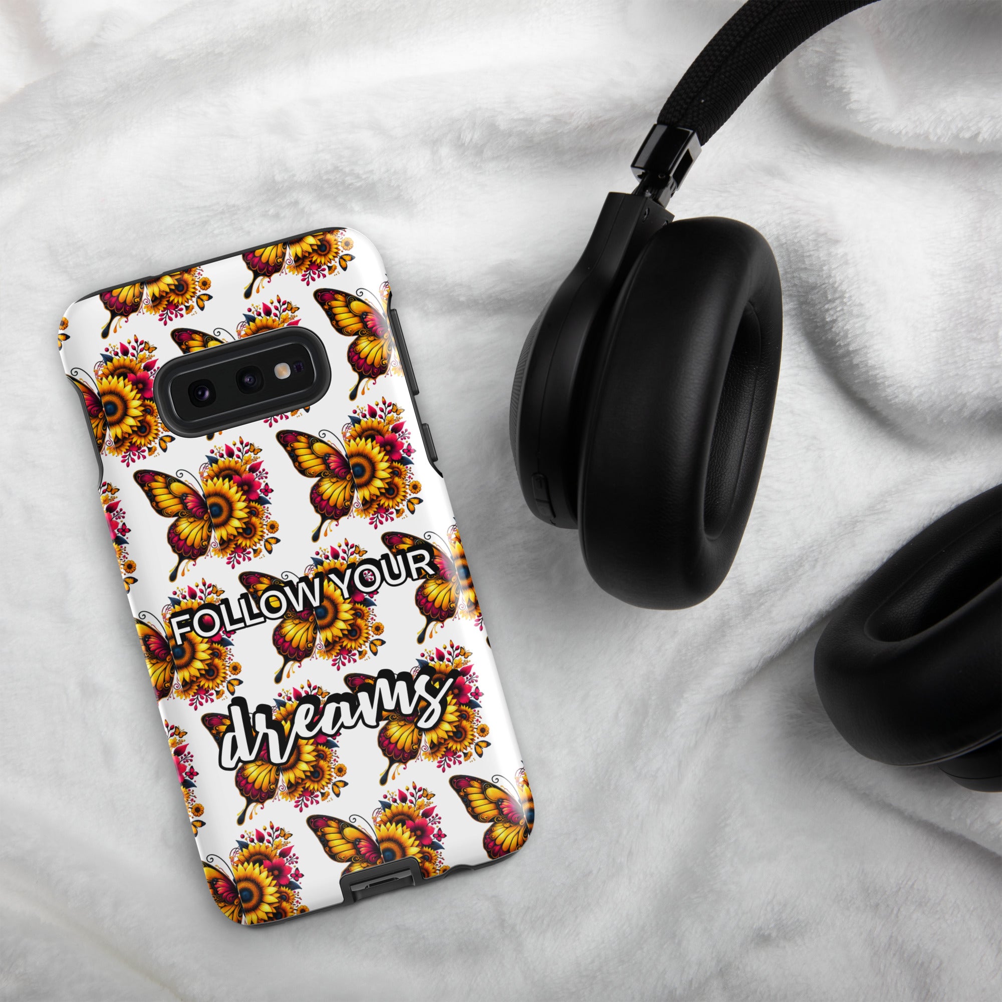 Phone case with butterfly design and 'Follow Your Dreams' text on a white surface with headphones.