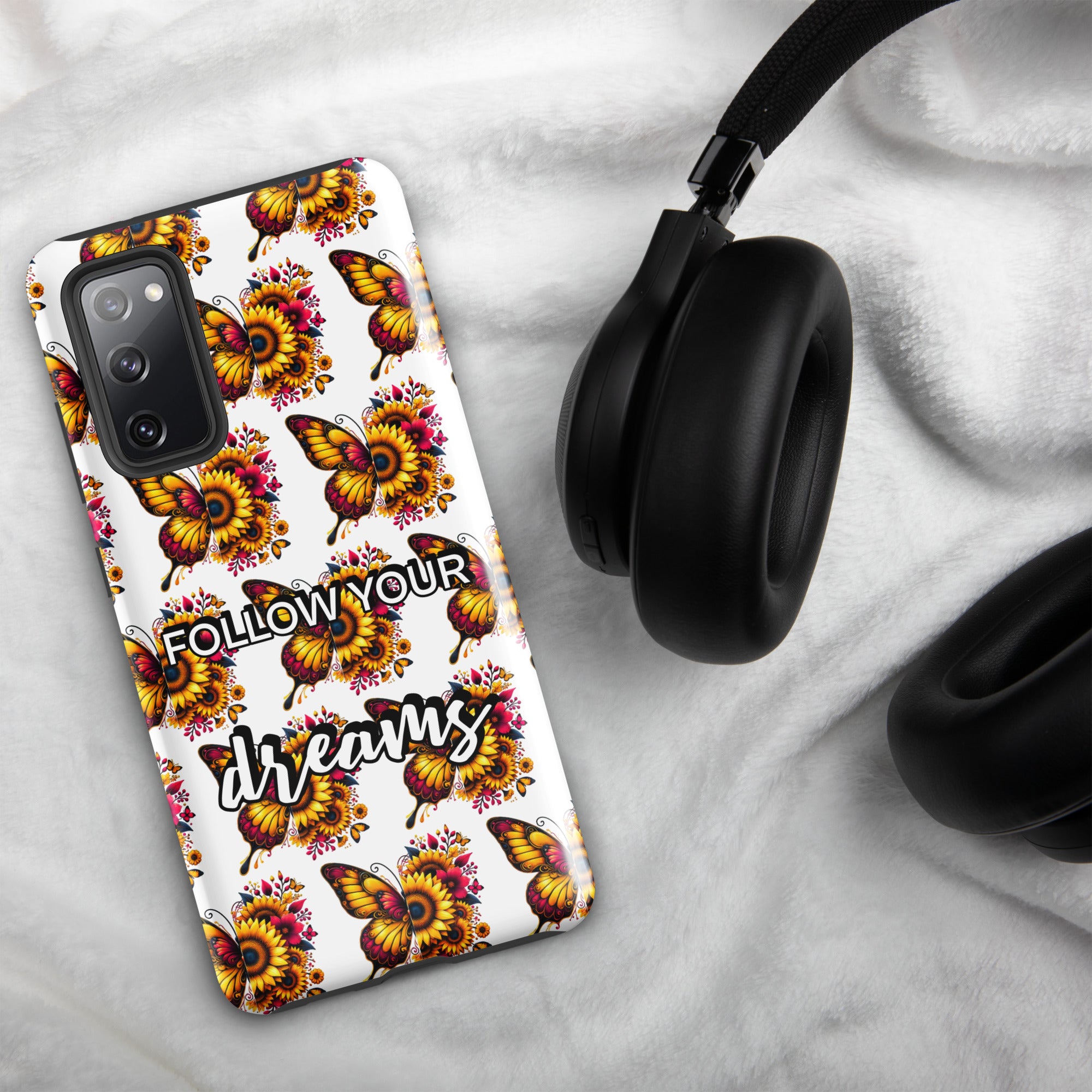 Phone case with butterfly design and 'Follow your dreams' text on a marble surface with headphones.