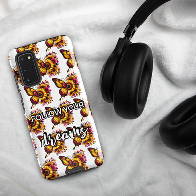 Phone case with butterfly design and 'Follow Your Dreams' text on a marble surface with headphones.