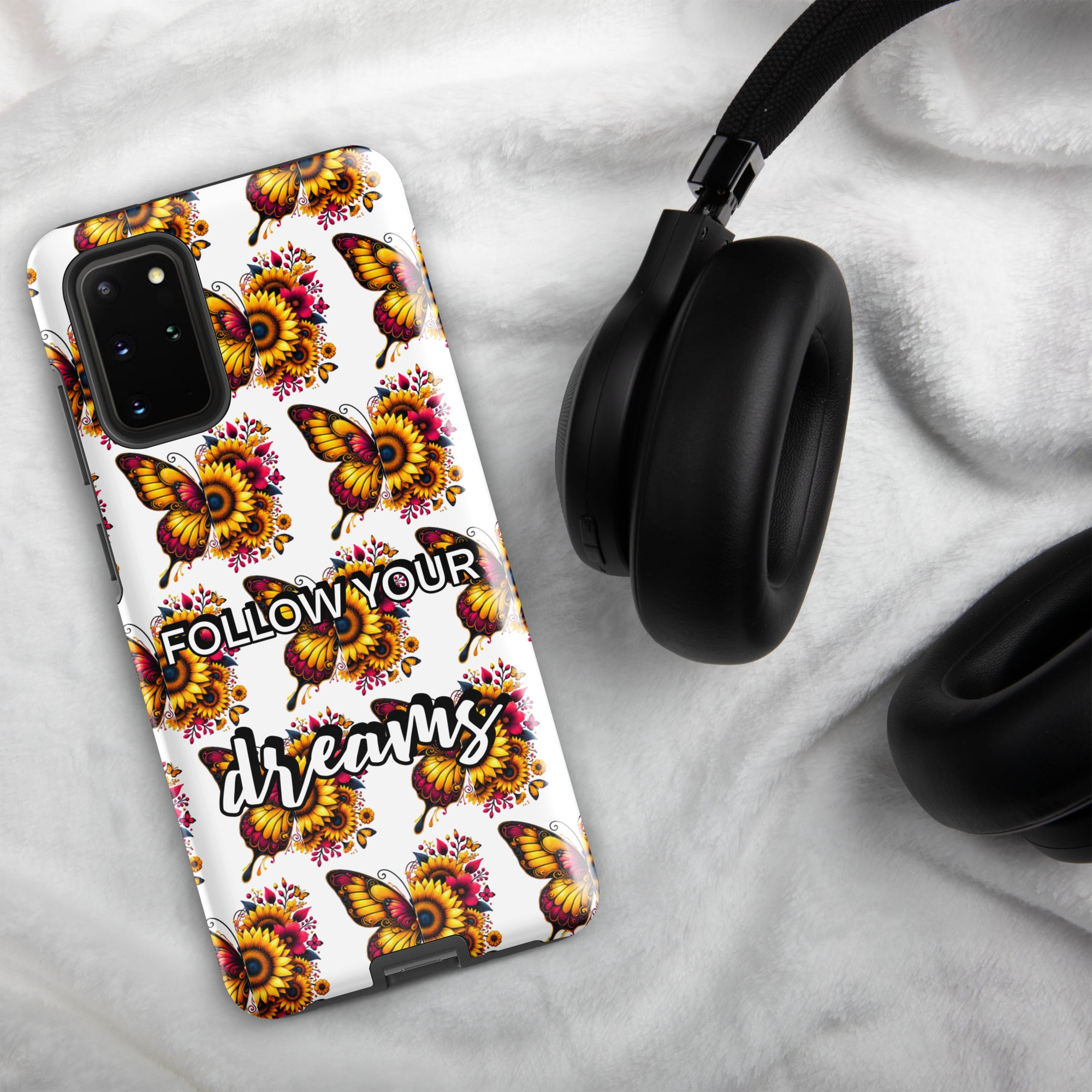 Phone case with butterfly design and 'Follow Your Dreams' text on a marble surface with headphones.
