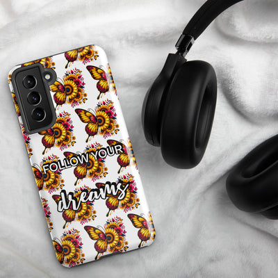 Phone case with butterfly design and 'Follow Your Dreams' text on a marble surface with headphones.