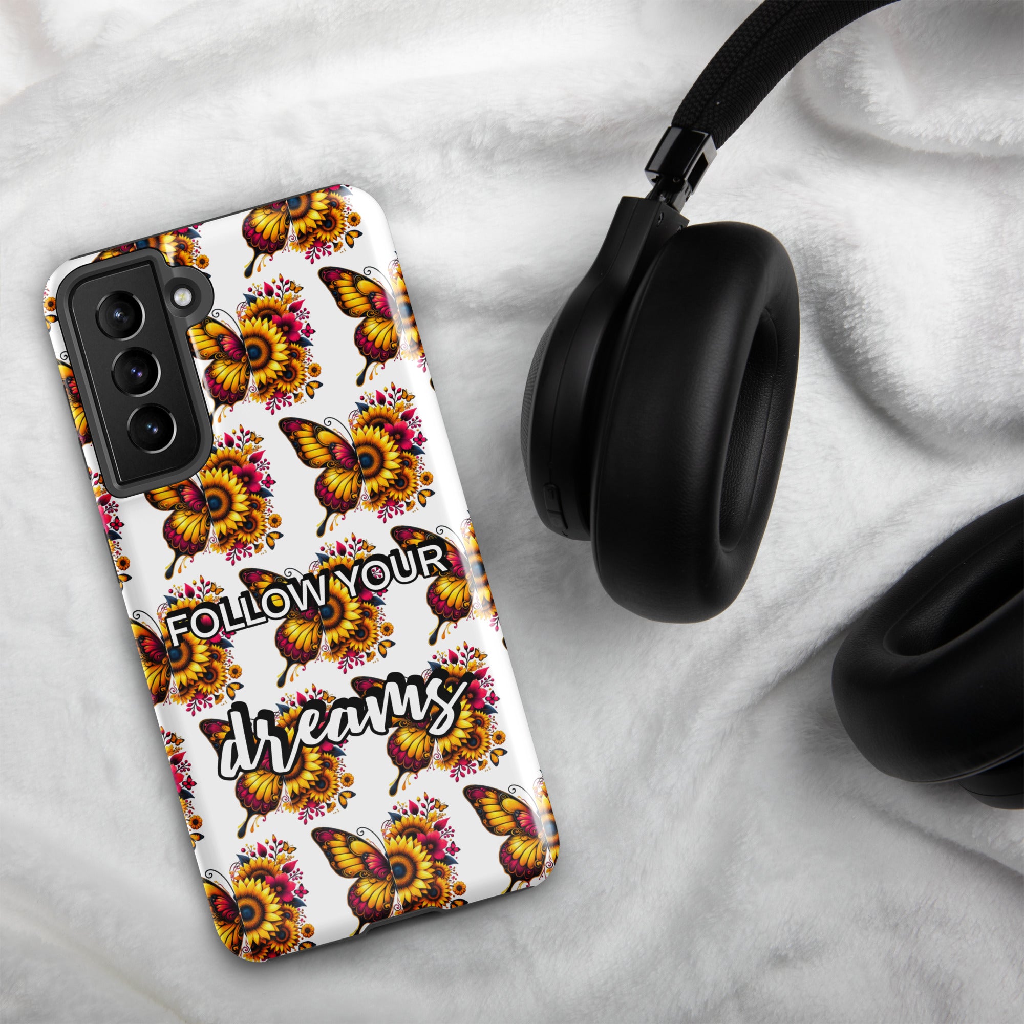 Phone case with butterfly design and 'Follow Your Dreams' text on a marble surface with headphones.