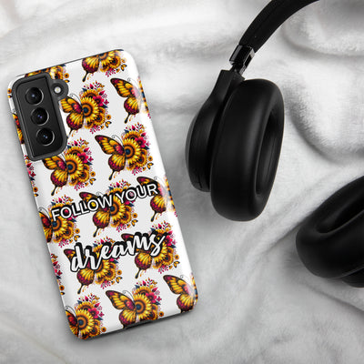 Phone case with butterfly design and 'Follow your dreams' text, next to black headphones on a light gray background