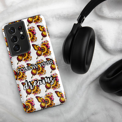 Phone case with butterfly design and 'Follow your dreams' text on a marble surface with headphones.