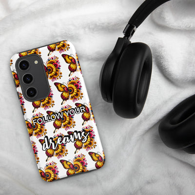 Phone case with butterfly design and 'Follow Your Dreams' text on a marble surface with headphones.