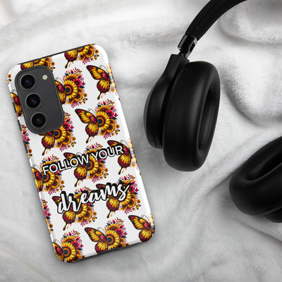 Phone case with butterfly design and 'Follow Your Dreams' text on a marble surface with headphones.