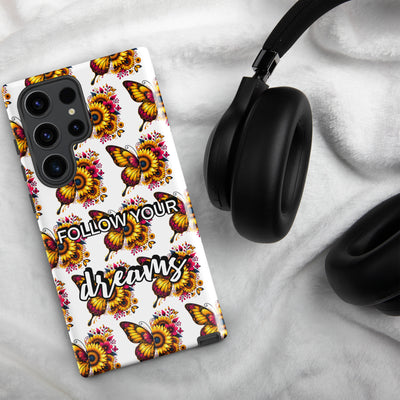 Phone case with butterfly and flower design and 'Follow Your Dreams' text on a marble surface with headphones.