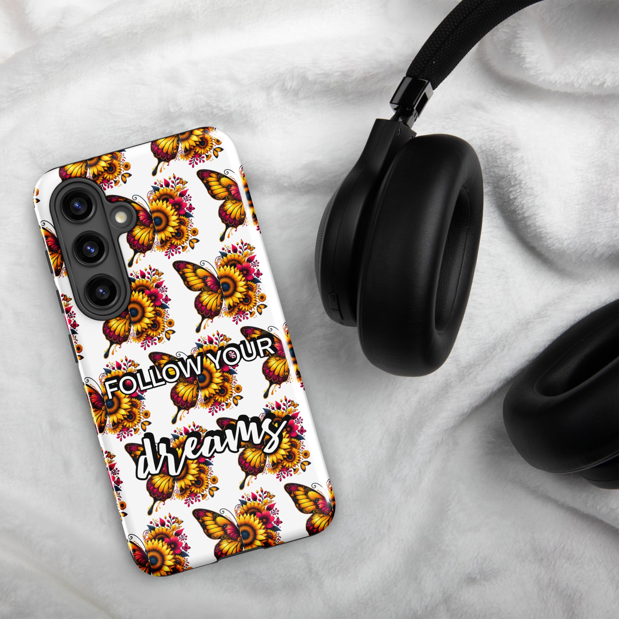 Phone case with butterfly design and 'Follow Your Dreams' text on a marble surface with headphones.