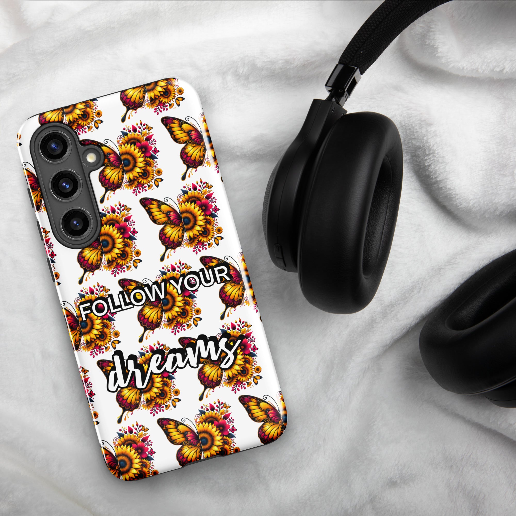 Phone case with butterfly design and 'Follow Your Dreams' text on a marble surface with headphones.