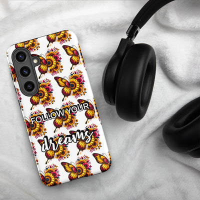 Phone case with butterfly design and 'Follow Your Dreams' text on a marble surface with headphones.