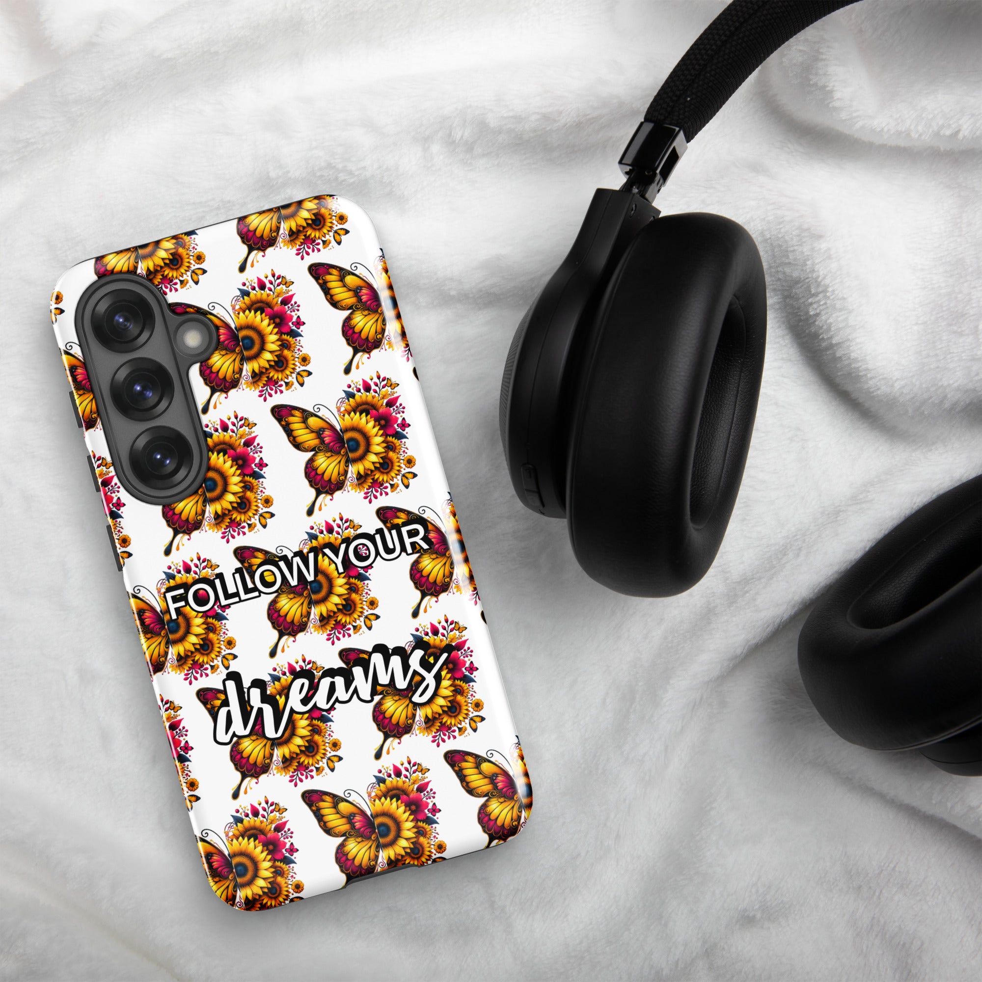 Phone case with butterfly design and 'Follow your dreams' text on a marble surface with headphones.