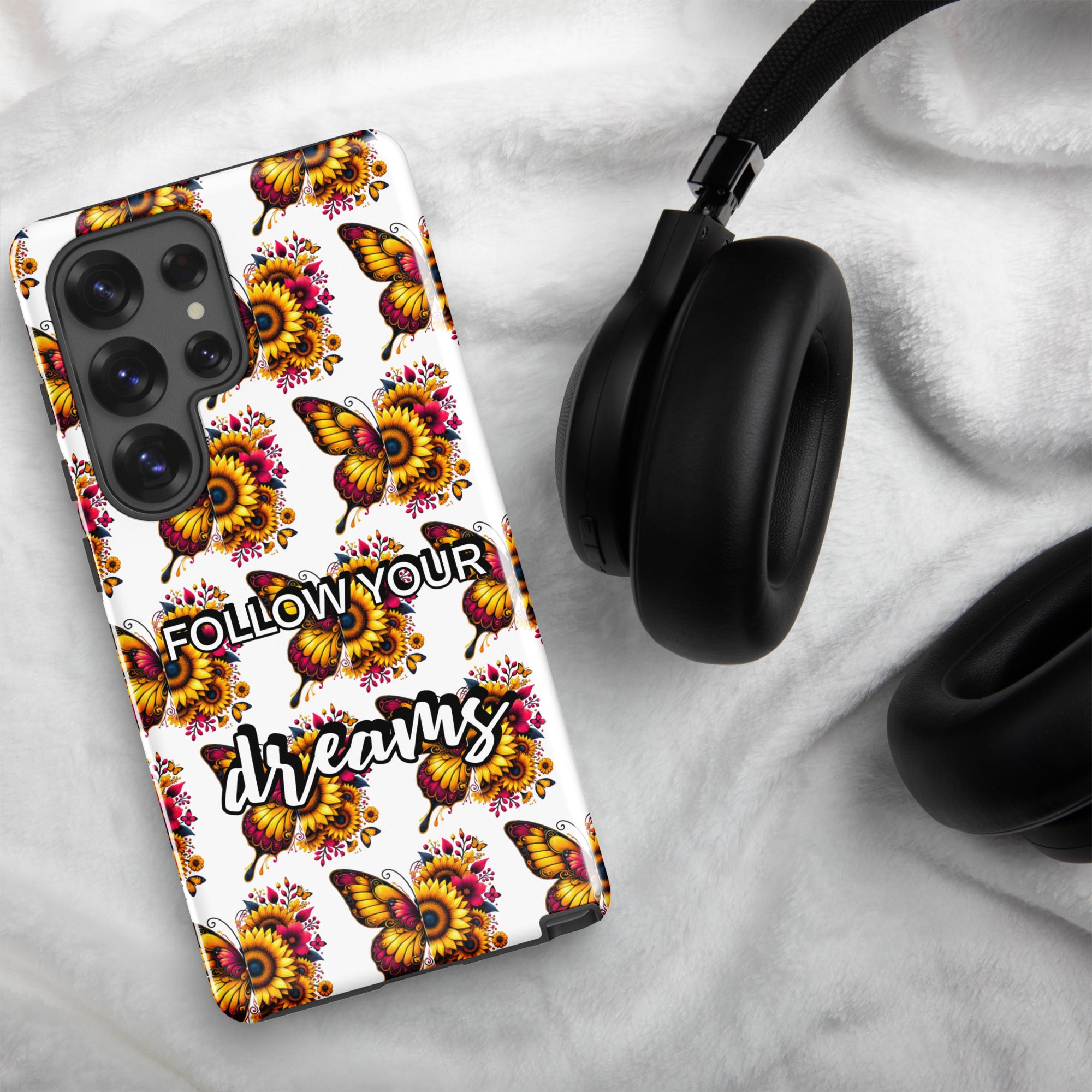 Phone case with butterfly design and 'Follow Your Dreams' text on a marble surface with headphones.