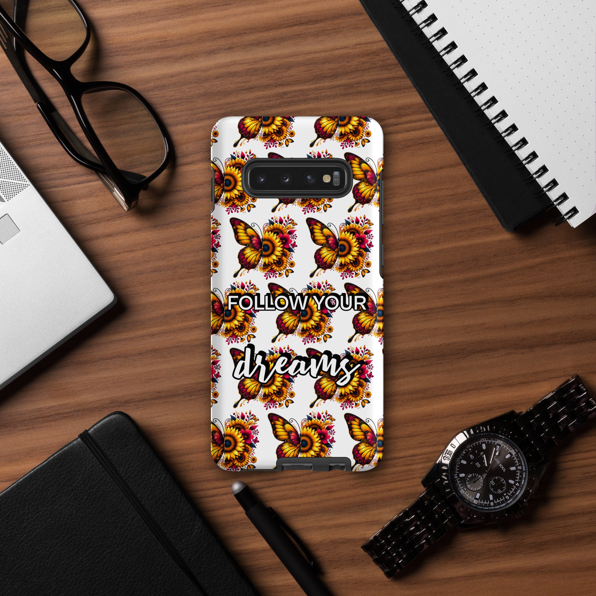 Phone case with butterfly design and 'Follow your dreams' text on a wooden desk with accessories.