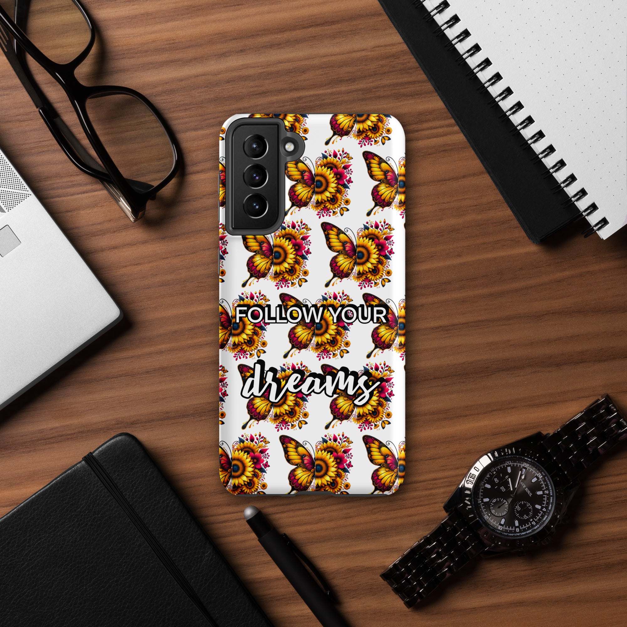 Phone case with butterfly design and 'Follow your dreams' text on a wooden desk with accessories.