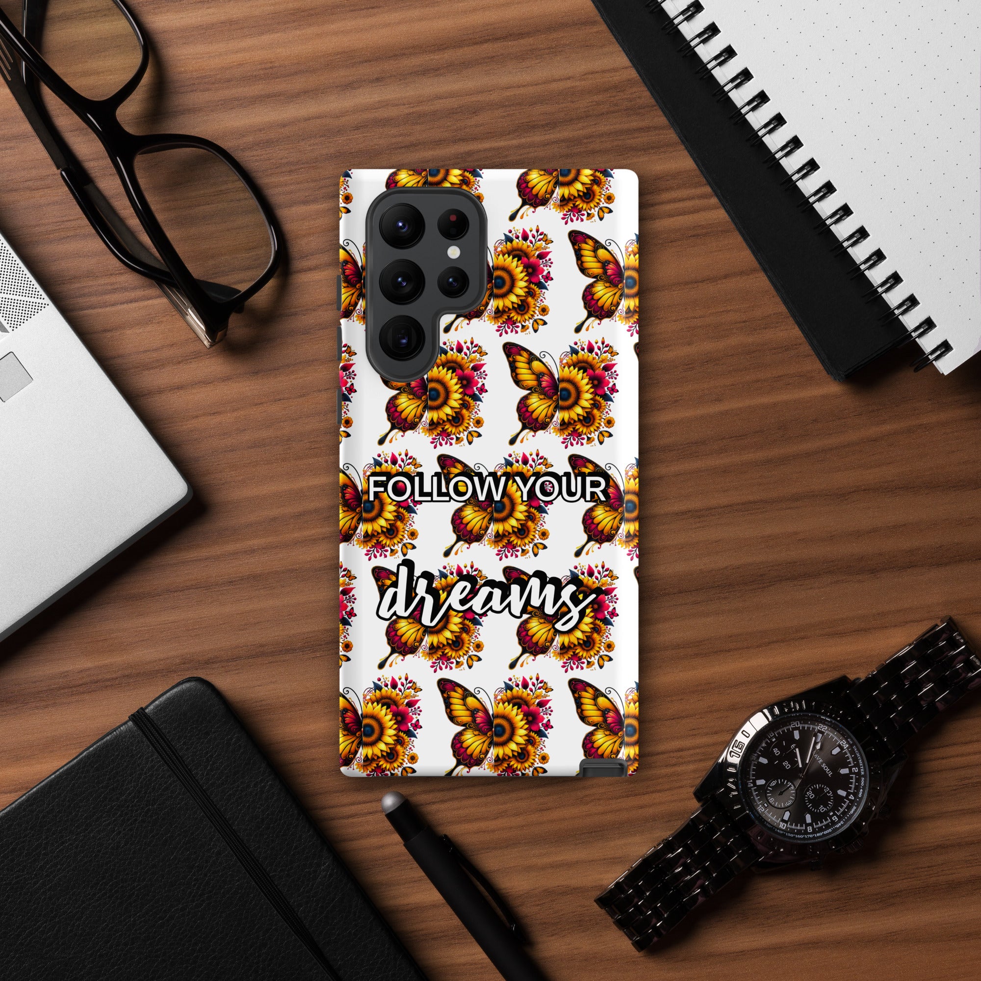 Phone case with butterfly design and 'Follow Your Dreams' text on a wooden desk.
