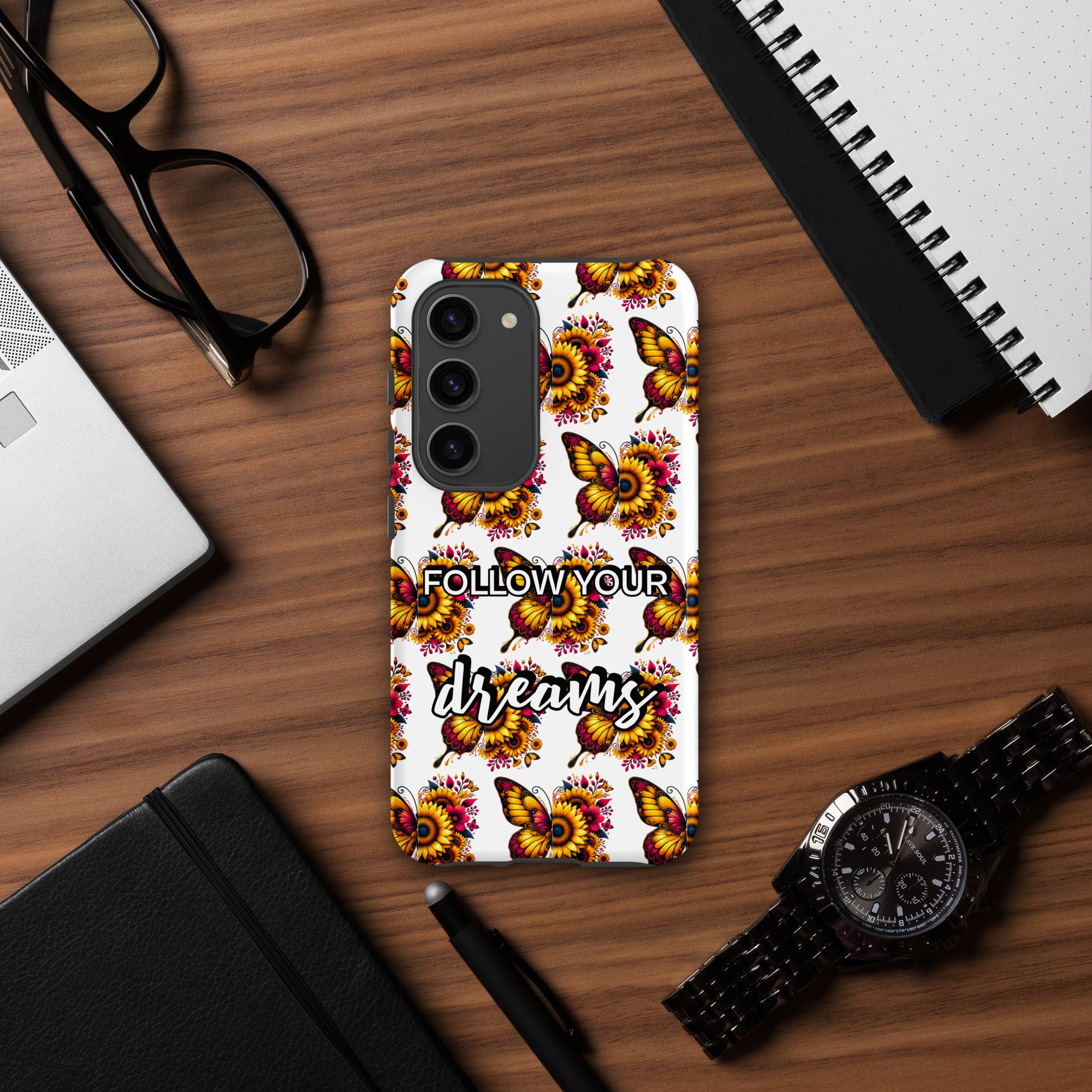 Phone case with butterfly design and 'Follow Your Dreams' text on a wooden desk.