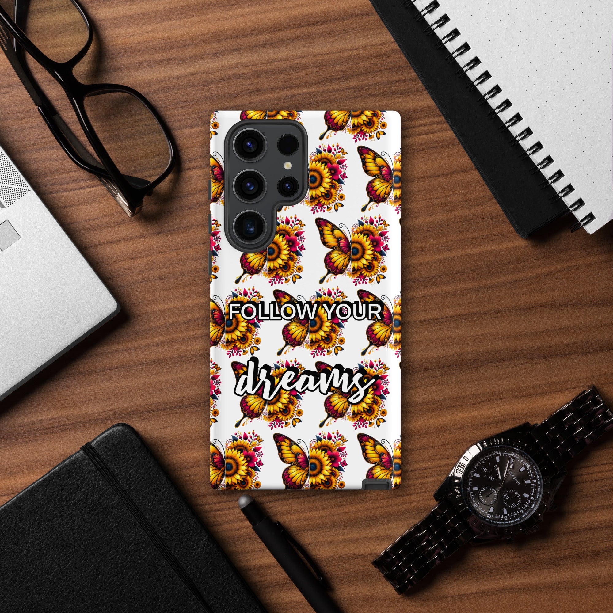 Phone case with butterfly design and 'Follow Your Dreams' text on a wooden desk.