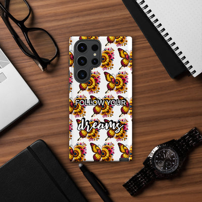 Phone case with butterfly design and 'Follow Your Dreams' text on a wooden desk.