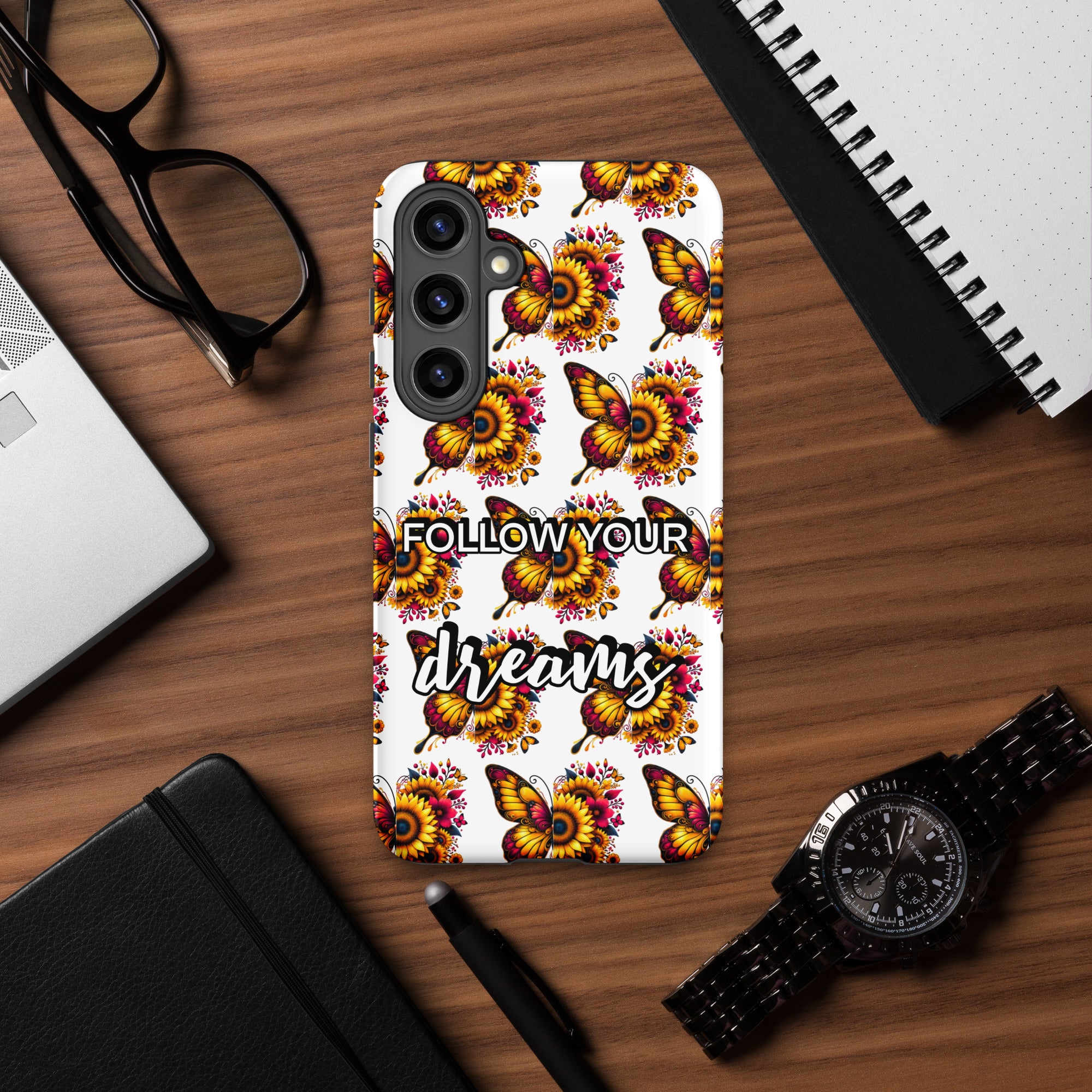 Phone case with butterfly design and 'Follow Your Dreams' text on a wooden desk.