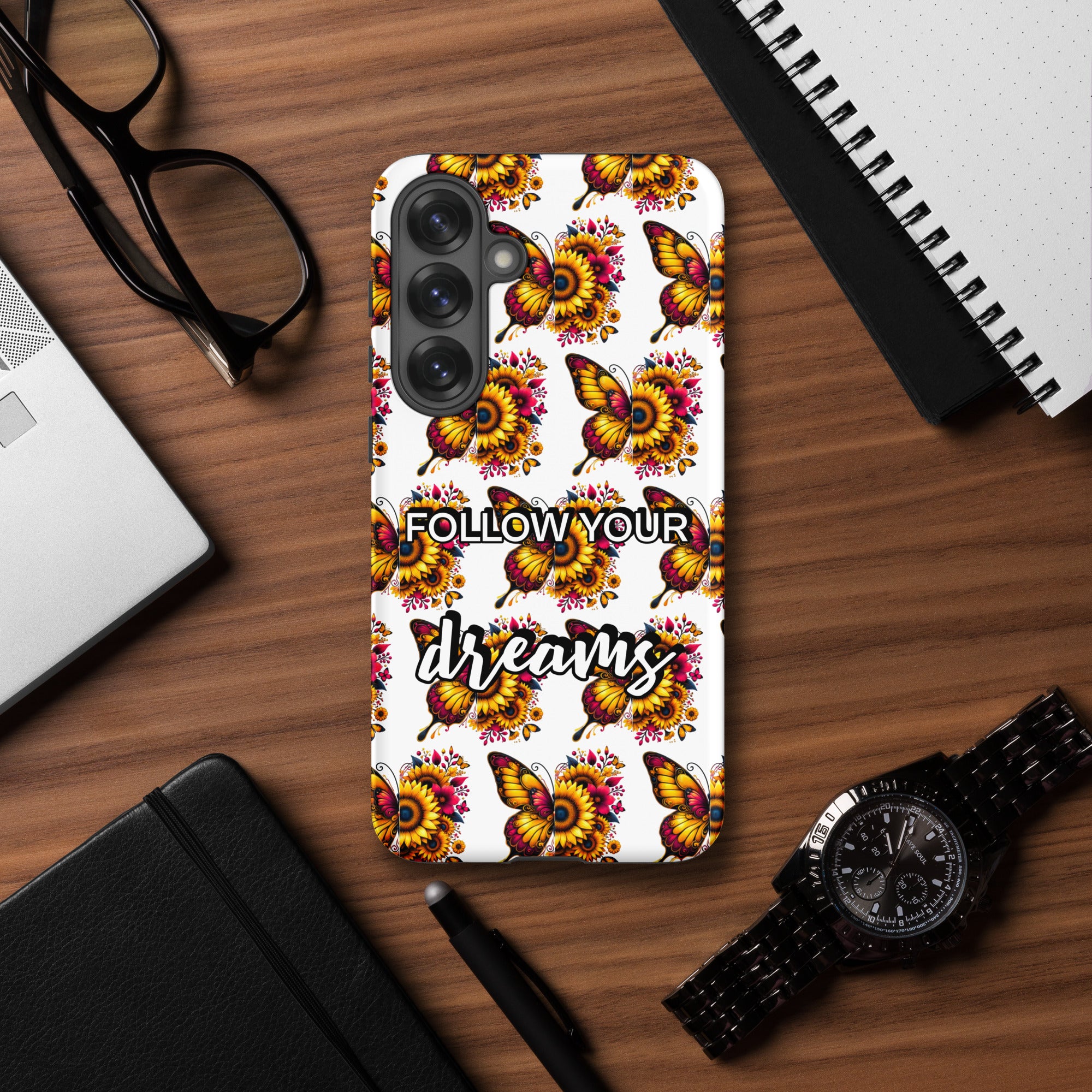 Phone case with butterfly design and 'Follow Your Dreams' text on a wooden desk with accessories.