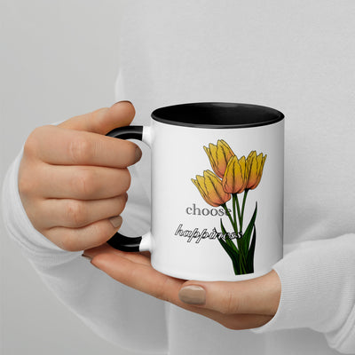 Hand holding a mug with yellow tulips and 'choose happiness' text on a light gray background