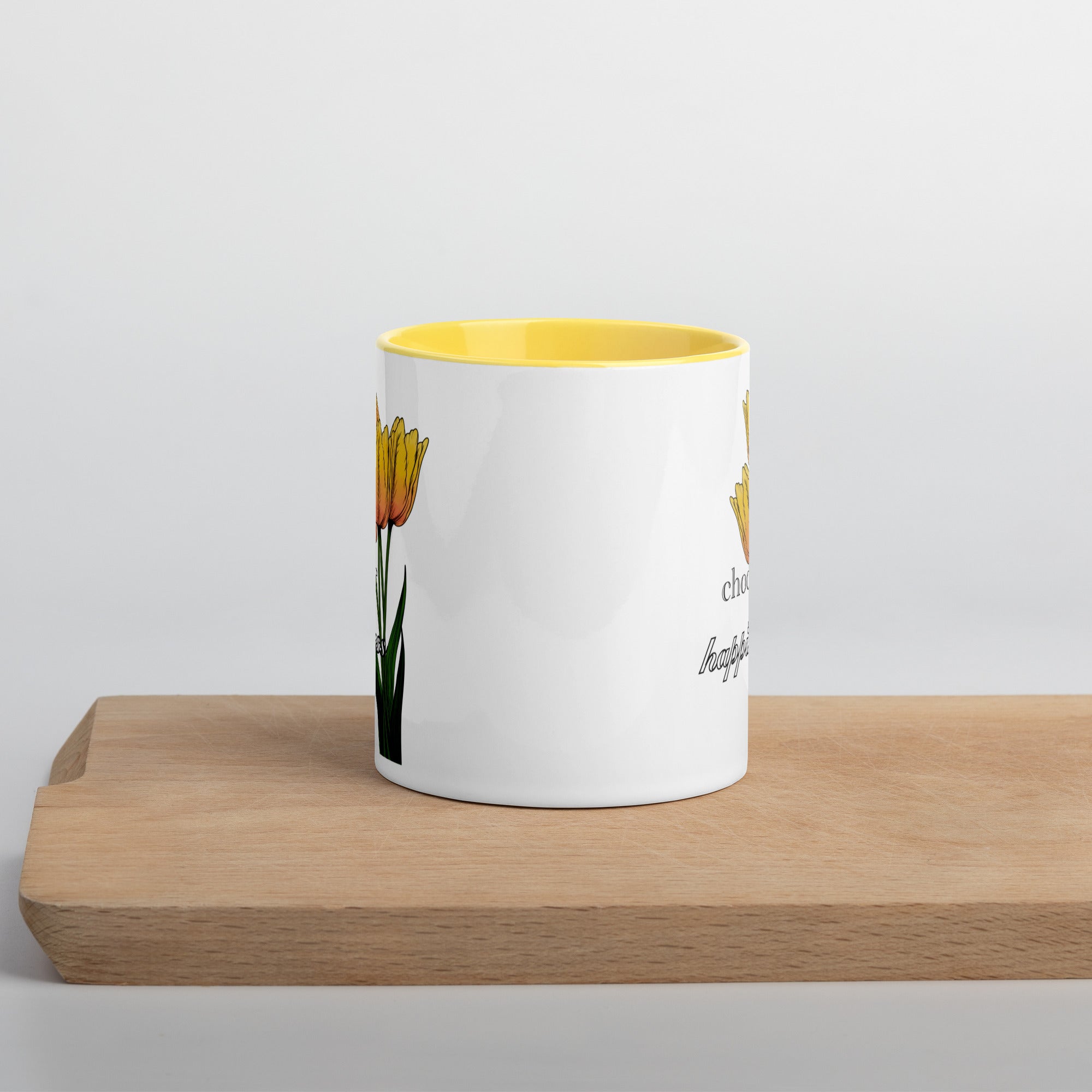 White mug with yellow interior and floral design on a wooden surface
