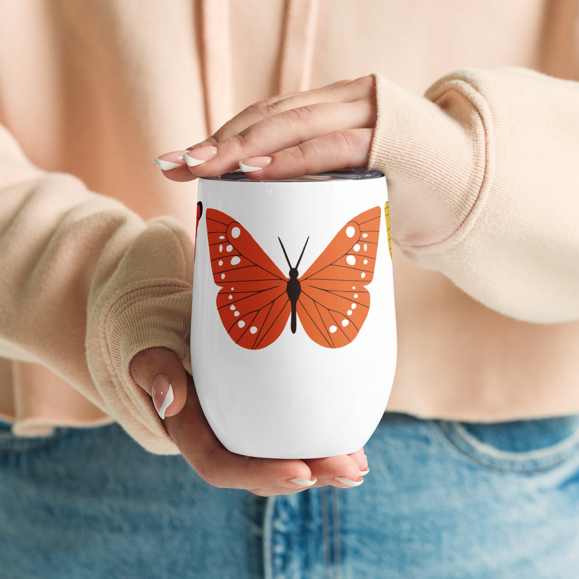 Person holding a white wine mug with a orange butterfly design, wearing a beige sweater and blue jeans.