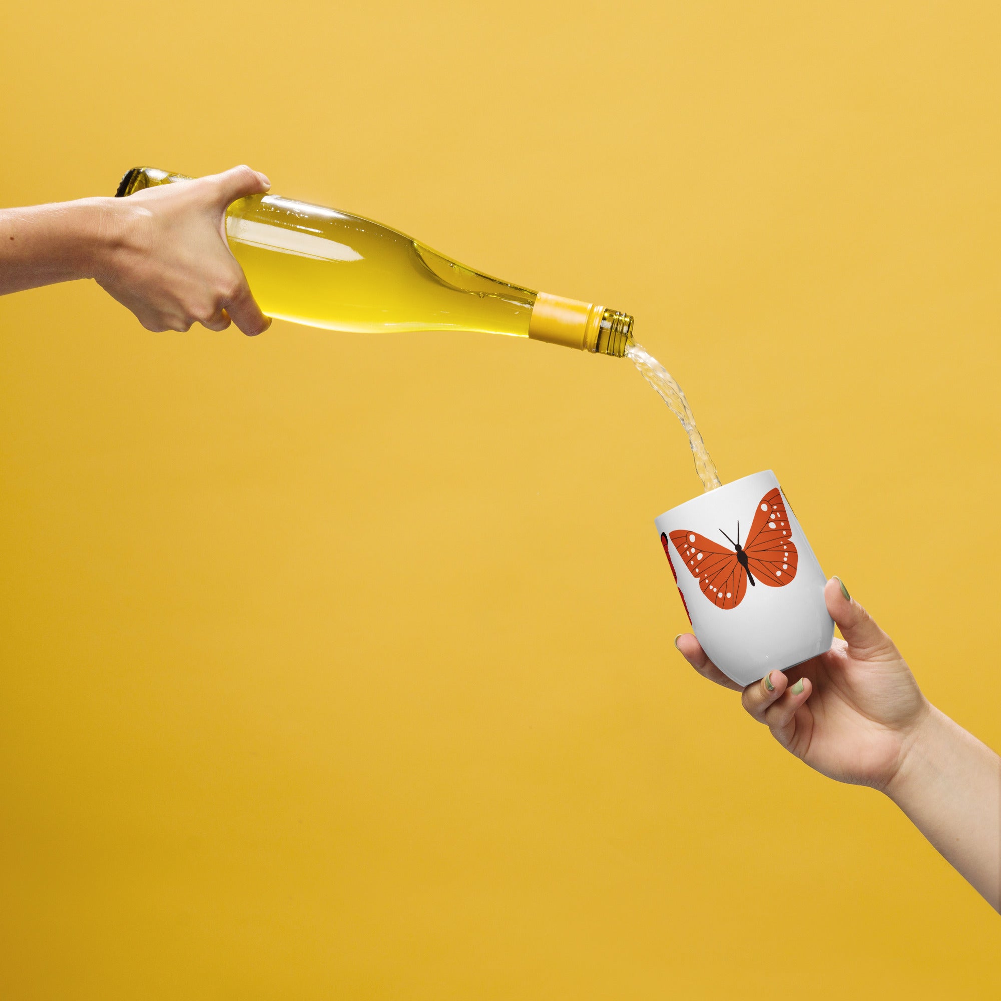 Person pouring white wine from a bottle into a cup with a butterfly design on a yellow background