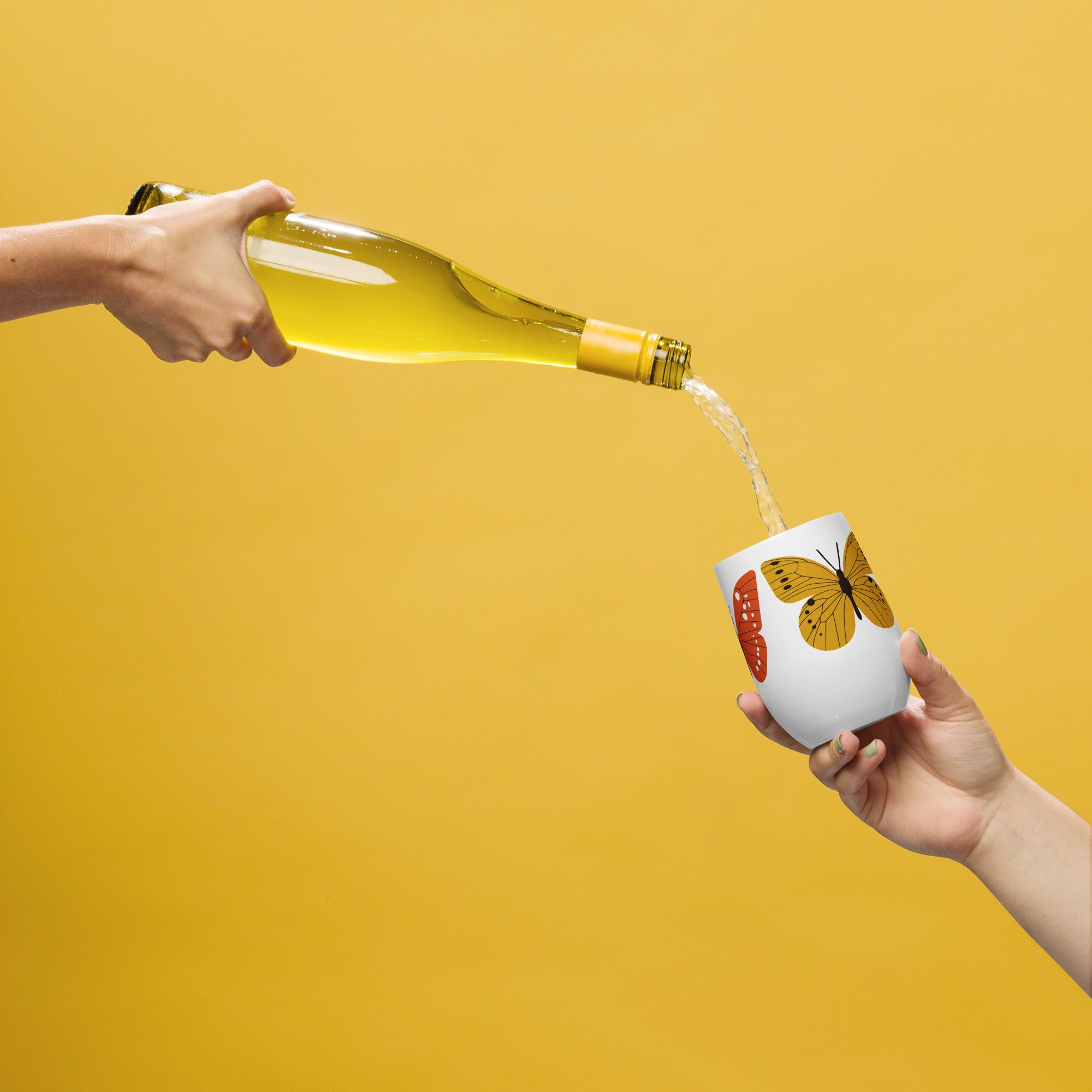 Person pouring white wine from a bottle into a white cup with a butterfly design on a yellow background