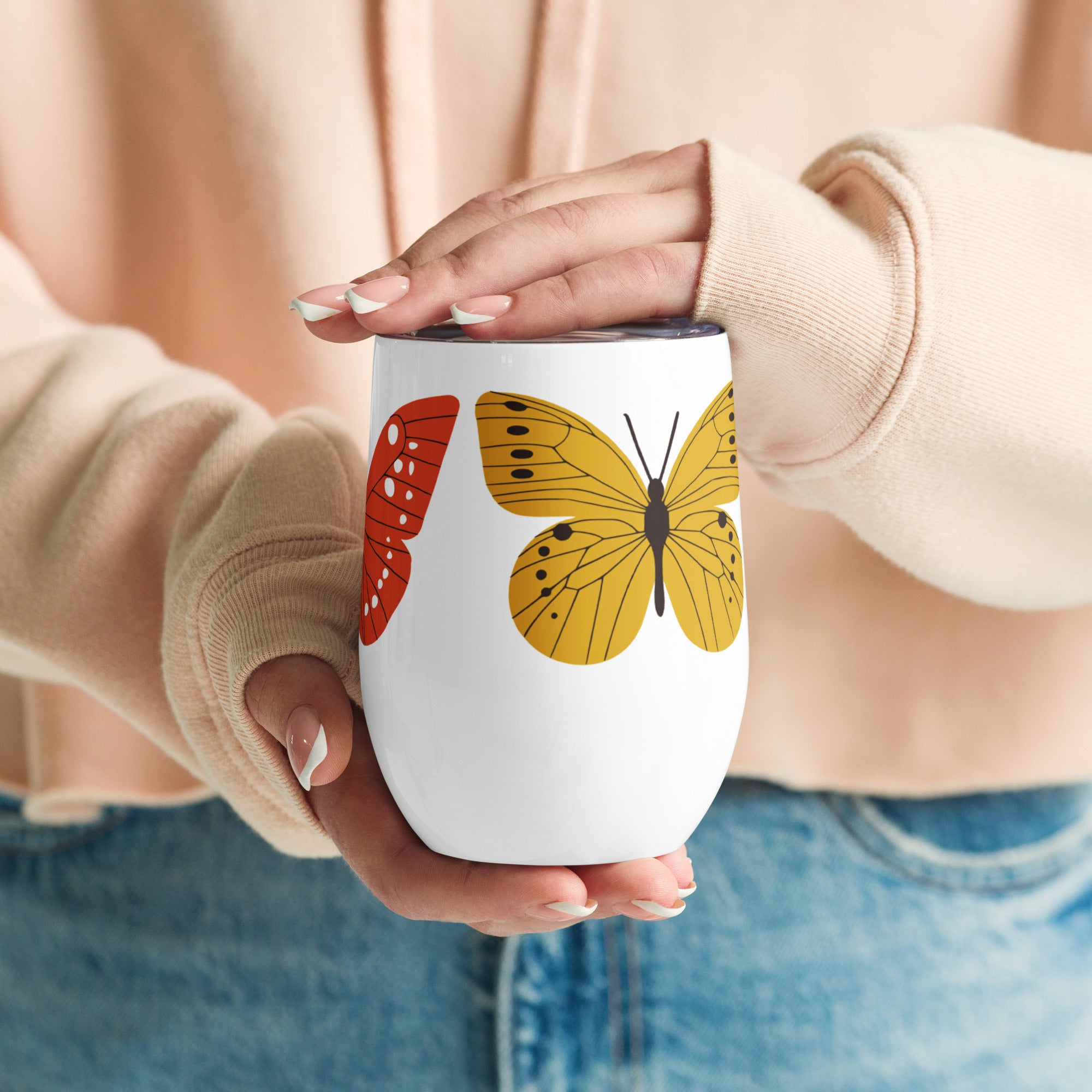 Person holding a white wine mug with a butterfly design, wearing a beige sweater and blue jeans.