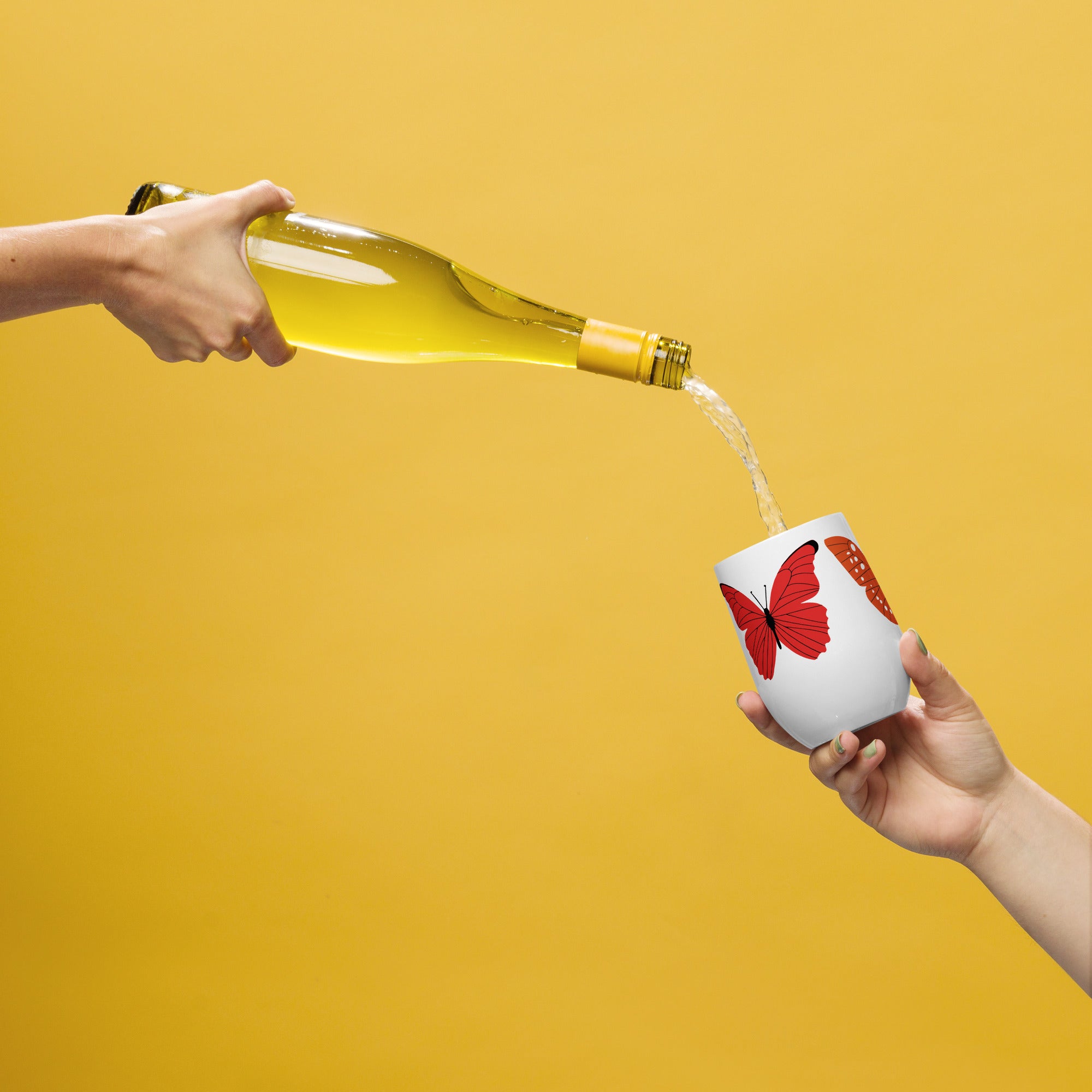 Person pouring white wine from a bottle into a white cup with red butterfly design on a yellow background