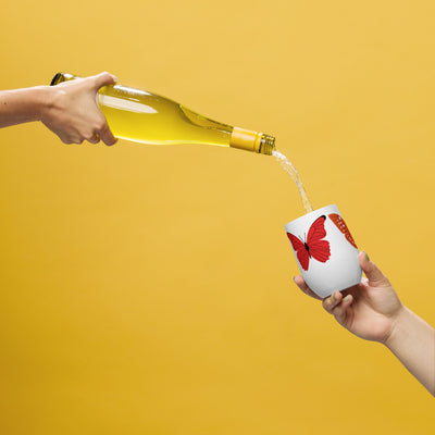 Person pouring white wine from a bottle into a white cup with red butterfly design on a yellow background