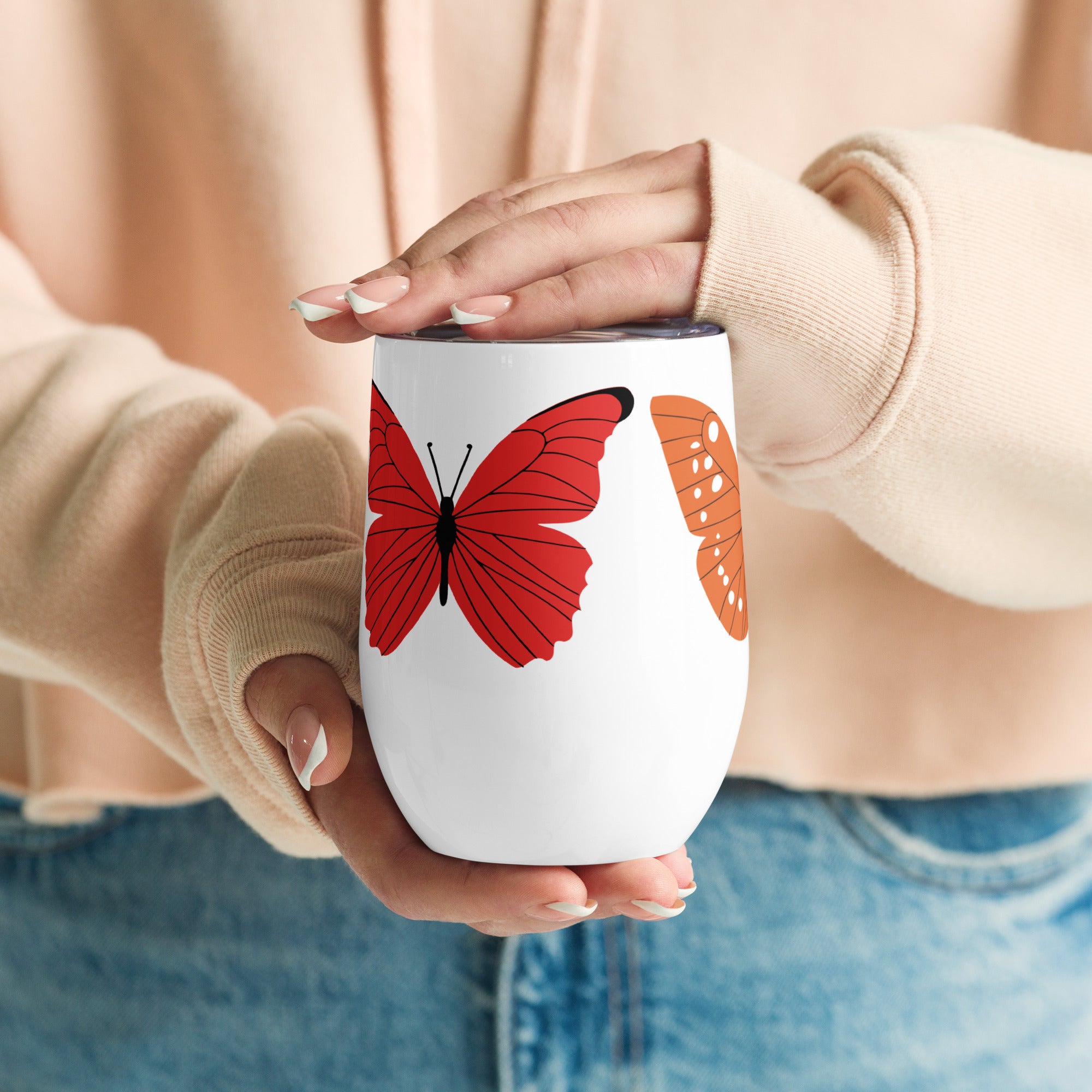 Person holding a white mug with butterfly design, wearing a beige sweater and blue jeans.