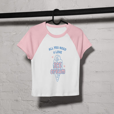 Pink and white baseball shirt with ice cream graphic and text on a hanger against a gray brick wall.