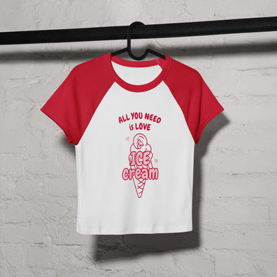 Red and white t-shirt with ice cream cone graphic and text on a hanger against a gray brick wall.