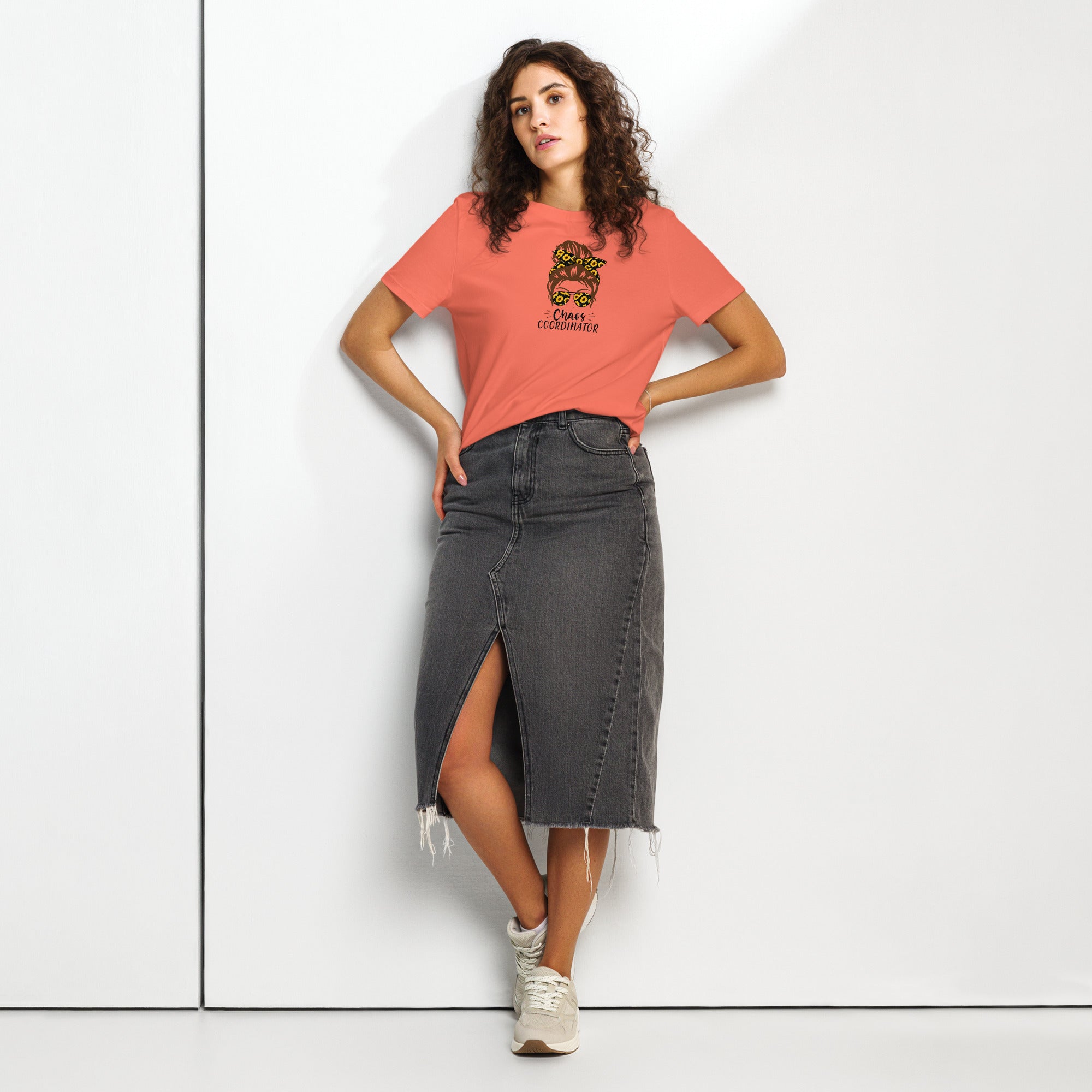 Woman wearing a coral t-shirt with a graphic girl design and 'Chaos Co-ordinator' text, a black denim skirt on a white background