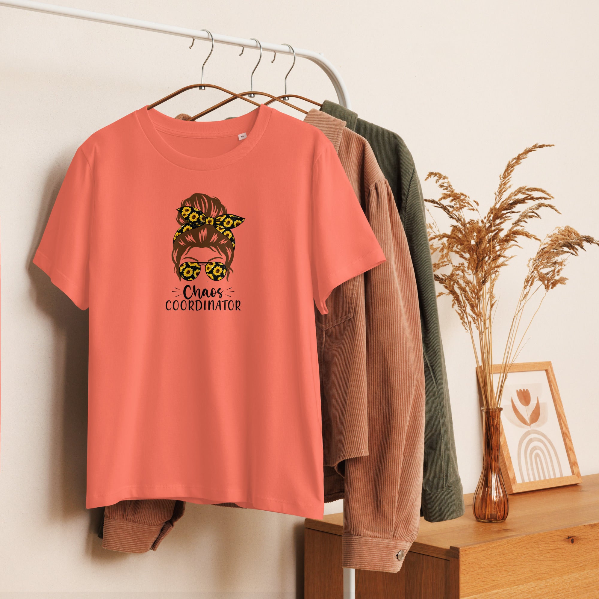 Coral t-shirt with graphic design hanging on a rack with other clothes.